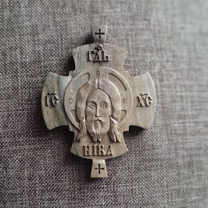 Könnte beinhalten: Ein Holzkreuz mit einem geschnitzten Bild von Jesus Christus in der Mitte. Das Kreuz ist mit den Worten "IC XC NIKA" in kyrillischer Schrift verziert.