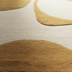May include: Close-up of a beige and gold area rug. The rug features a textured, looped pile with a pattern of large, abstract shapes in a warm gold color against a neutral beige background. The design creates a soft, inviting aesthetic.