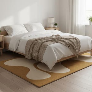 May include: A modern bedroom scene featuring a bed with white linens and a tan knitted throw. A mustard yellow and cream-colored abstract rug sits on the floor. The room has light wood furniture and a white wall.