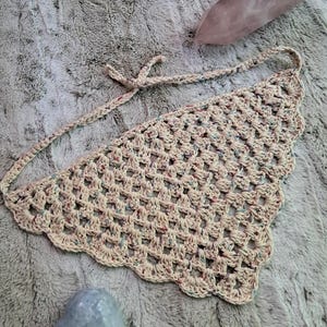 May include: A crocheted beige triangle scarf with multicolored yarn accents. The scarf has a scalloped edge and is tied with a bow.