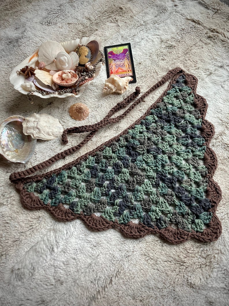 Detailed view of the handmade crochet work on the Aphrodite Shell Hair Bandana, highlighting the fine craftsmanship and unique shell edge. The color option is Forest, a green multicolored triangle with brown edging and ties.