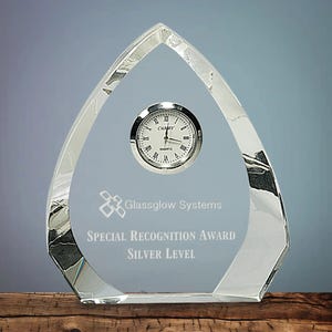 Peut inclure: Un trophée en verre transparent en forme de goutte d'eau avec un cadran d'horloge argenté. Le trophée porte l'inscription "Glassglow Systems" et "Special Recognition Award Silver Level". L'horloge indique "CAMRY QUARTZ".