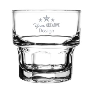 May include: A clear, stackable glass tumbler with a wide base and a thick, textured bottom. The glass features the text "Your CREATIVE Design" with star accents. The design is etched into the glass, creating a subtle, elegant look.