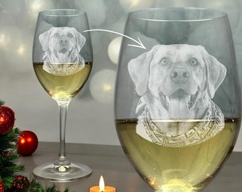 Könnte beinhalten: Zwei klare Weingläser, gefüllt mit Weißwein, jeweils mit einem detaillierten Bild eines Hundegesichts graviert. Die Gläser stehen auf einem Tisch mit Weihnachtsdekorationen, darunter rote Ornamente und eine brennende Kerze.