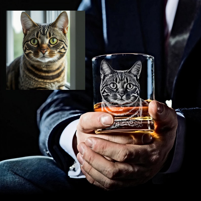 Puede incluir: Un vaso de vidrio transparente con la cara de un gato grabada. El gato es un atigrado con rayas negras y un pecho blanco. El vaso est&aacute; lleno de un l&iacute;quido dorado.