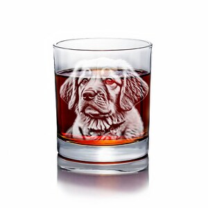 Puede incluir: Un vaso de vidrio transparente lleno de un l&iacute;quido &aacute;mbar oscuro. Una silueta blanca de la cabeza de un perro est&aacute; grabada en el vidrio.