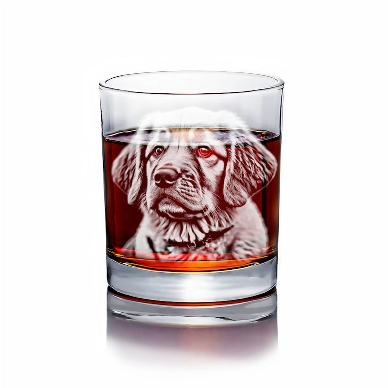 Puede incluir: Un vaso de vidrio transparente lleno de un l&iacute;quido &aacute;mbar oscuro. Una silueta blanca de la cabeza de un perro est&aacute; grabada en el vidrio.