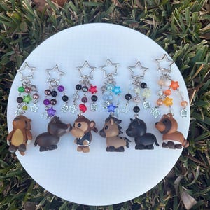 May include: A collection of seven animal-themed keychains. Each keychain features a small, detailed animal figurine, such as a bear, pig, monkey, and horse, hanging from a silver chain with colorful beads and a star-shaped clasp.