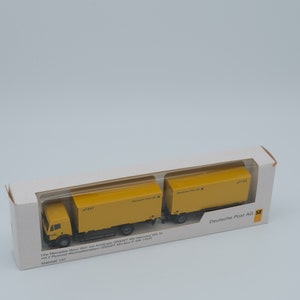 May include: A yellow Deutsche Post AG model truck with two trailers, presented in a white box. The model is a Mercedes-Benz 1831 with GRAAFF MV-Hercules WA 18 trailers. The box has text in German.