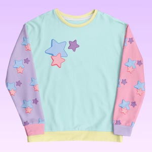 May include: A light blue sweatshirt with a yellow trim around the neck and cuffs. The sleeves are a split design with one side featuring a purple background with pink and blue stars and the other side featuring a pink background with pink and blue stars.