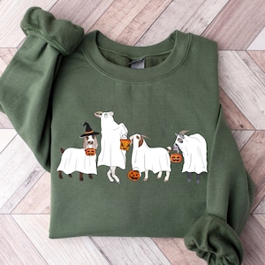May include: A dark green sweatshirt featuring a Halloween-themed graphic. The graphic depicts a dog and three goats dressed as ghosts, each holding a jack-o'-lantern. The dog wears a witch hat. The sweatshirt is made of a soft material.