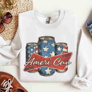 May include: White sweatshirt with a graphic of three red, white, and blue cans with stars and stripes. The text "Ameri Can" is printed in red and white on a red banner.