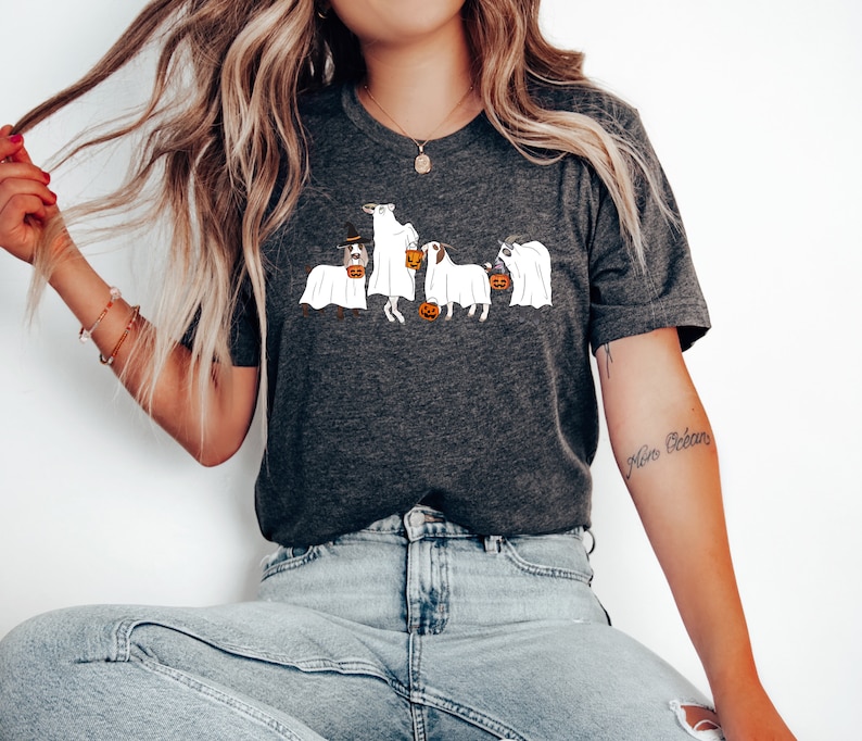 May include: Dark gray t-shirt featuring a Halloween-themed design. The graphic depicts four dogs dressed as ghosts, each holding a jack-o'-lantern. One dog wears a witch's hat. A fun and festive design for dog lovers.