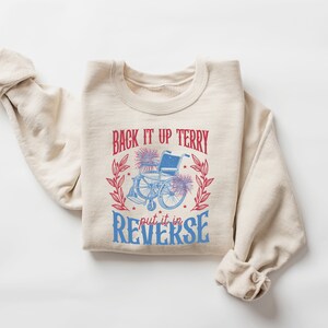 May include: A beige sweatshirt with a graphic print of a wheelchair with fireworks and the text "Back it up Terry put it in reverse".
