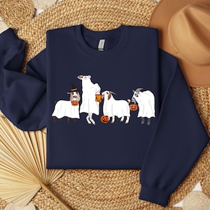 May include: Navy blue sweatshirt featuring a Halloween-themed design. The graphic depicts four goats dressed as ghosts, each holding a jack-o'-lantern. One goat wears a witch hat. The design is in white, orange, and black.