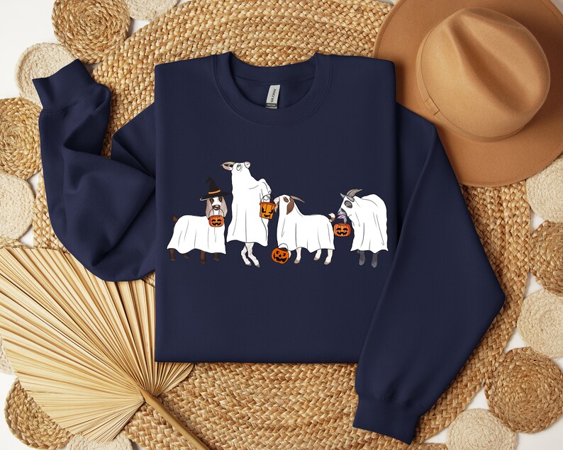 May include: Navy blue sweatshirt featuring a Halloween-themed design. The graphic depicts four goats dressed as ghosts, each holding a jack-o'-lantern. One goat wears a witch hat. The design is in white, orange, and black.