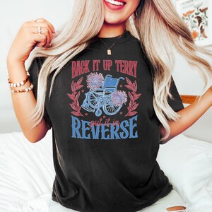 May include: Black t-shirt with a red and blue graphic design featuring a wheelchair with flowers and the text "Back it up Terry put it in reverse."