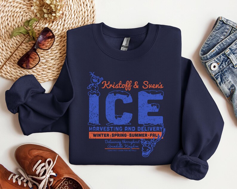 May include: Navy blue sweatshirt with a graphic featuring the text "Kristoff & Sven's ICE" in blue and orange. The design includes Olaf and Sven characters, with "Harvesting and Delivery" and seasonal references.