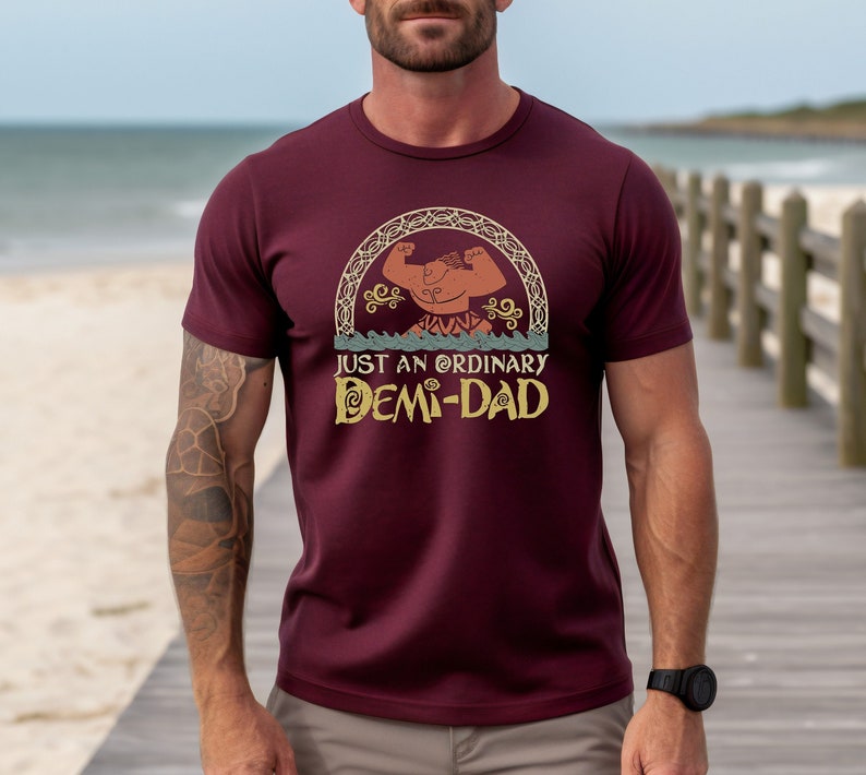 K&ouml;nnte beinhalten: Ein maroonfarbenes T-Shirt mit einem Comic-Charakter-Motiv und dem Text "Just an ordinary Demi-Dad".