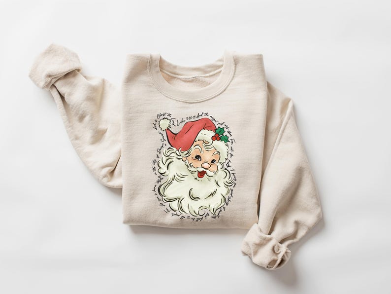 Pu&ograve; includere: Felpa girocollo beige con grafica vintage di Babbo Natale. L'illustrazione di Babbo Natale ha un cappello rosso, barba bianca e accenti di agrifoglio. Il testo circonda l'immagine. Un top comodo a maniche lunghe per le festivit&agrave;.