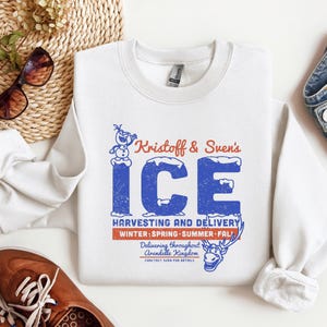 May include: White crewneck sweatshirt with a blue and red graphic. The graphic reads "Kristoff & Sven's ICE" with text below indicating "Harvesting and Delivery" and "Winter, Spring, Summer, Fall".