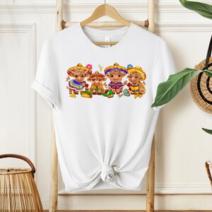 May include: White t-shirt with a graphic of four brown cows wearing colorful sombreros and traditional Mexican clothing. The cows are holding tacos and maracas.