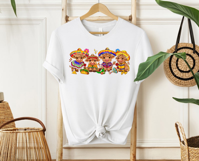 May include: White t-shirt with a graphic of four brown cows wearing colorful sombreros and traditional Mexican clothing. The cows are holding tacos and maracas.