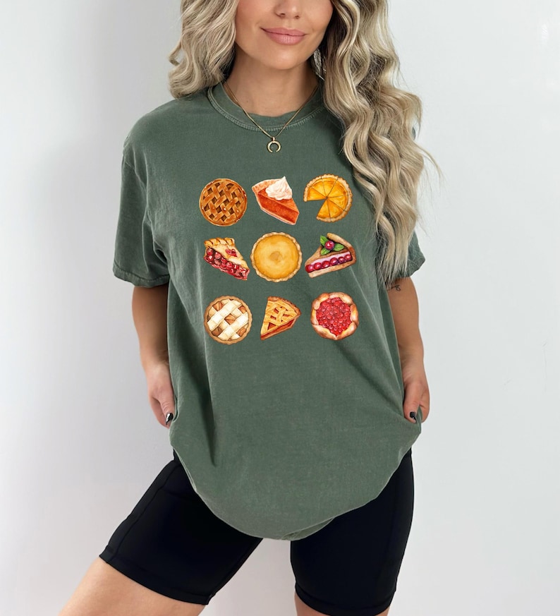 May include: Green t-shirt featuring a watercolor illustration of various pies. The design includes whole pies and slices, showcasing different fillings and crusts. The shirt is a comfortable, casual style.