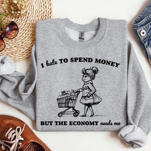 May include: A gray sweatshirt with the text "I hate to spend money but the economy needs me" and a black and white illustration of a person pushing a shopping cart.