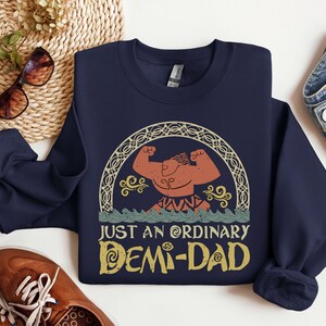 K&ouml;nnte beinhalten: Navyblauer Sweatshirt mit einem Grafikdruck einer muskul&ouml;sen Figur mit einem Lorbeerkranz und dem Text "Just an ordinary Demi-Dad".