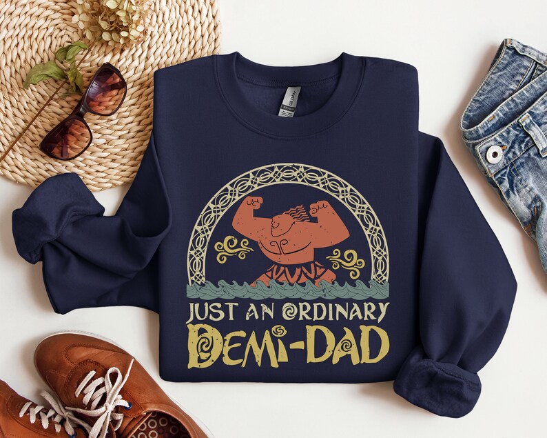 K&ouml;nnte beinhalten: Navyblauer Sweatshirt mit einem Grafikdruck einer muskul&ouml;sen Figur mit einem Lorbeerkranz und dem Text "Just an ordinary Demi-Dad".