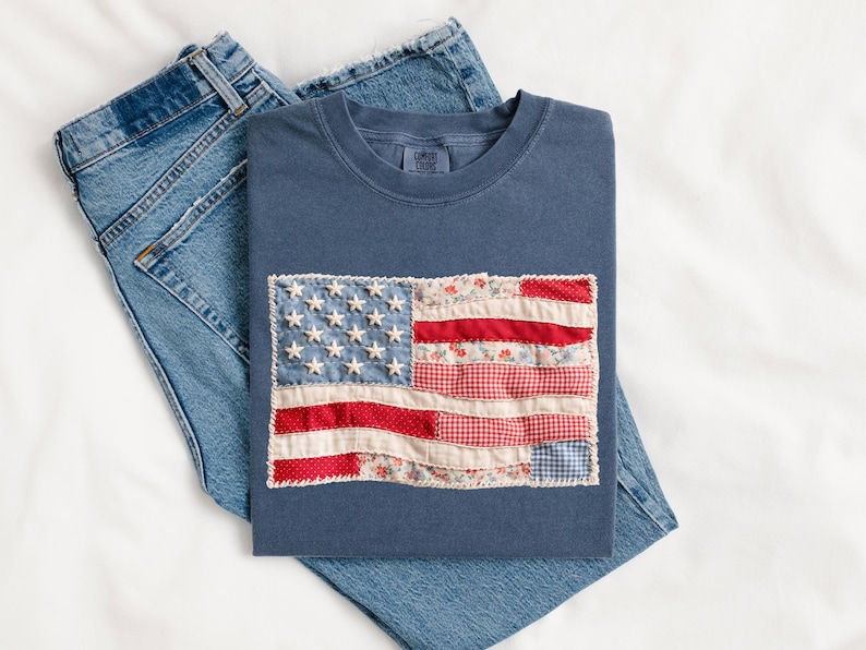 Peut inclure: Un t-shirt bleu marine avec un drapeau am&eacute;ricain en patchwork, pli&eacute; sur un jean bleu. Le drapeau pr&eacute;sente des &eacute;toiles blanches et des rayures rouges et &agrave; motifs floraux. Le t-shirt est en mati&egrave;re souple.