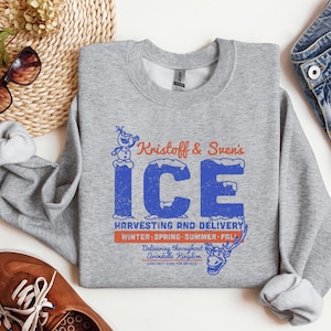 May include: A heather gray sweatshirt with the text "Kristoff & Sven's ICE" in blue and orange. The sweatshirt also features a graphic of Olaf and Sven, with the words "Harvesting and Delivery" and "Winter, Spring, Summer, Fall."