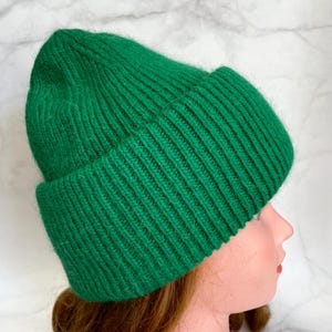 May include: A bright green knit beanie hat with a folded brim. The hat is made of a ribbed knit material. The hat is shown on a mannequin head with red hair.