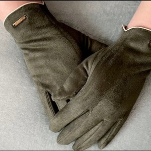 May include: A pair of olive green suede gloves with a white trim and a small brown button detail on each glove.