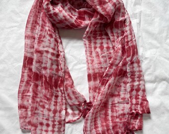 Peut inclure: Écharpe tie-dye rouge et blanche avec des pompons aux extrémités. Le motif de l'écharpe est à rayures verticales. Les pompons sont d'une nuance de rouge plus foncée.
