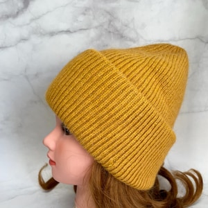 May include: A mustard yellow knitted beanie hat. The hat is made of a soft, ribbed fabric.