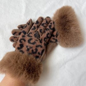 May include: Brown leather gloves with a leopard print pattern and brown fur trim. The gloves are shown on a hand.