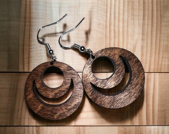 Puede incluir: Un par de pendientes de madera con un diseño de luna creciente. Los pendientes son marrones y tienen ganchos plateados.