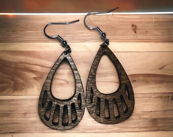 Puede incluir: Un par de pendientes de madera en forma de lágrima con un diseño de huella de pata de oso. Los pendientes son marrones con una mancha marrón oscura y tienen ganchos plateados.