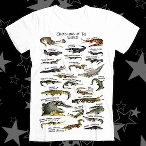 Op de afbeelding: Een wit T-shirt met een afbeelding van verschillende soorten krokodillen en alligators van over de hele wereld. De afbeelding heeft de titel "Crocodilians of the World".