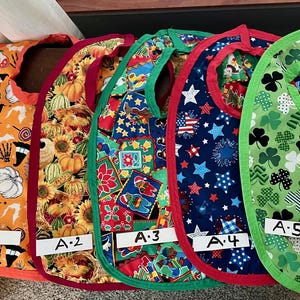 May include: Five different patterned bibs with red, green, and blue trim. The bibs are labeled A-1, A-2, A-3, A-4, and A-5.