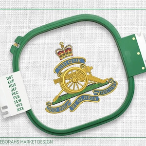 Könnte beinhalten: Ein grüner Stickrahmen mit weißem Stoffhintergrund. Der Stoff hat ein gesticktes Design mit einer goldenen Kanone, über der sich eine Krone befindet. Der Text "UBIQUE QUO FAS ET GLORIA DUCUNT" ist um die Kanone gestickt. Der Text "DST EXP HUS JEF PEC PES SEW VP3 XXX" ist auf einem weißen Etikett gedruckt.