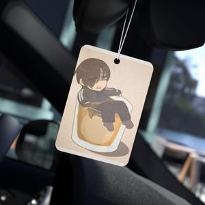 May include: Rectangular car air freshener with a cartoon illustration of a character sitting in a glass of liquid. The air freshener is beige with a black hole at the top for hanging. The character is wearing a black tracksuit.