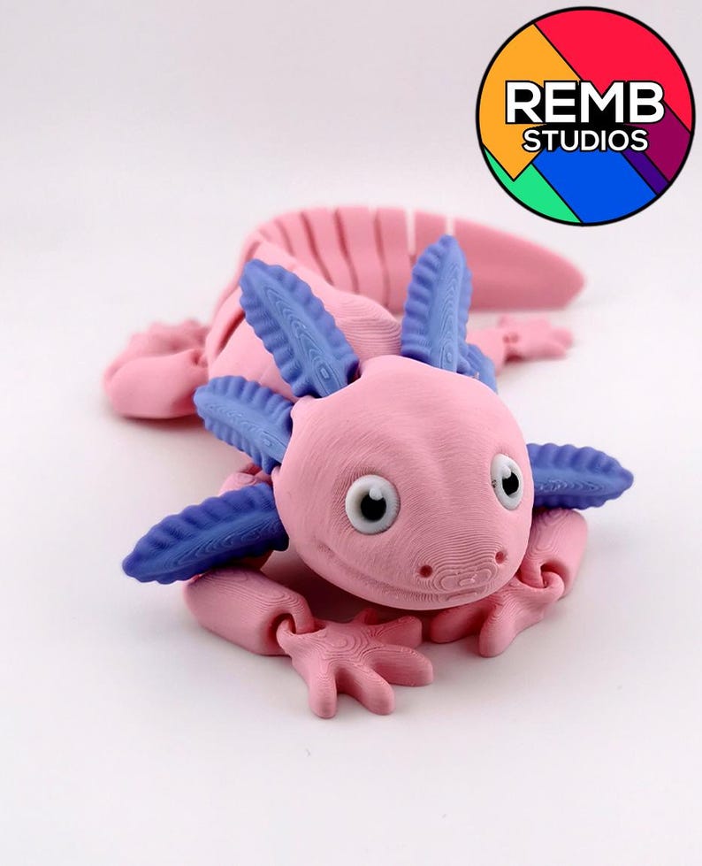 May include: A pink axolotl figurine with blue gills and limbs. The figurine has a detailed, textured surface and large, round eyes. The REMB STUDIOS logo is in the upper right corner.