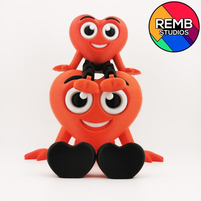 Puede incluir: Dos figuras rojas en forma de coraz&oacute;n con caras sonrientes y ojos grandes. El coraz&oacute;n m&aacute;s peque&ntilde;o est&aacute; sentado encima del coraz&oacute;n m&aacute;s grande. Ambas figuras tienen pies en forma de coraz&oacute;n negros. El coraz&oacute;n m&aacute;s peque&ntilde;o tiene brazos y piernas negros. El coraz&oacute;n m&aacute;s grande tiene pies negros. El fondo es blanco. REMB STUDIOS est&aacute; escrito en un c&iacute;rculo colorido en la esquina superior derecha de la imagen.
