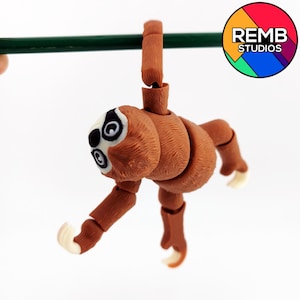 May include: A brown and white sloth figurine hanging from a green branch. The sloth has articulated limbs and is posed in a hanging position. The figurine is made of plastic and has a realistic appearance.