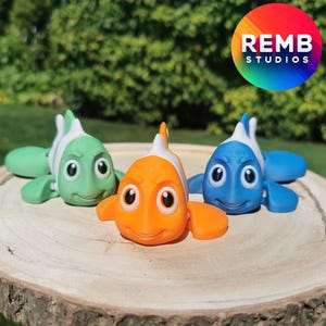 May include: Three colorful toy fish with white bellies and black eyes. The fish are green, orange, and blue. The fish are on a wooden surface.