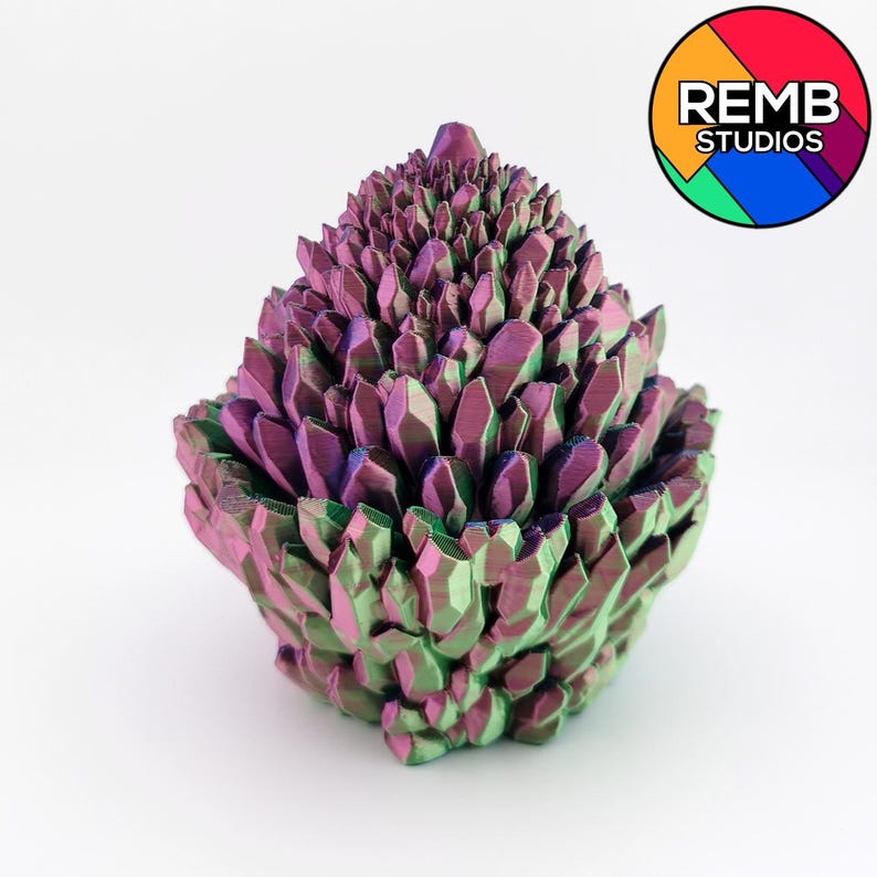 May include: A 3D-printed sculpture of a cluster of crystals in shades of purple, green, and blue. The crystals are arranged in a layered, geometric pattern, creating a textured surface. The sculpture has a rounded base and a pointed top. The REMB STUDIOS logo is in the upper right corner.