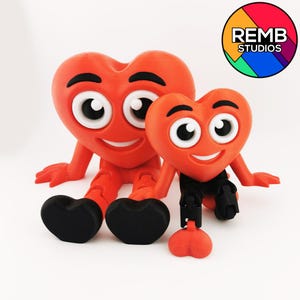 Puede incluir: Dos figuras rojas en forma de coraz&oacute;n con caras sonrientes y ojos grandes. El coraz&oacute;n m&aacute;s grande est&aacute; sentado con las piernas cruzadas, mientras que el coraz&oacute;n m&aacute;s peque&ntilde;o est&aacute; sentado con las piernas estiradas. Ambas figuras tienen brazos y piernas negros. El coraz&oacute;n m&aacute;s grande tiene un pie en forma de coraz&oacute;n negro en cada pie. El coraz&oacute;n m&aacute;s peque&ntilde;o tiene un pie en forma de coraz&oacute;n negro en cada pie y una cola en forma de coraz&oacute;n negro.